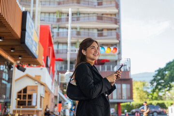 Asian professional businesswoman holding cellphone using smartphone standing or walking on big city urban street outside. Successful Asian business woman