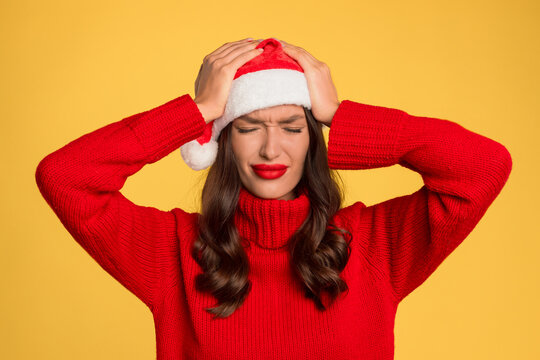 woman in Santa hat suffering with headache against yellow backdrop