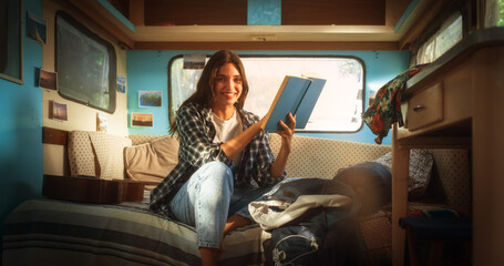 Beautiful Girl Relaxing in a Camper Van, Sitting on a Bed and Reading an Adventure Novel Book....