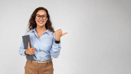 Cheerful caucasian young businesswoman professional with tablet, points finger on copy space
