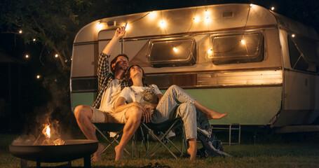 Young Beautiful Couple Relaxing at a Caravan Camping Area in the Evening, Keeping Warm with...