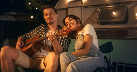 Portrait of a Happy Couple Spending Time at a Campfire, Playing Guitar Music and Singing Funny...