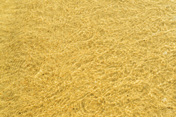 Sea water over golden sand. Glares of light on the sandy bottom. Crystal clear water on the beach.