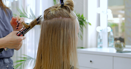 Fototapeta premium Close-up view of stylist hairdresser making hairstyle using curling tongs