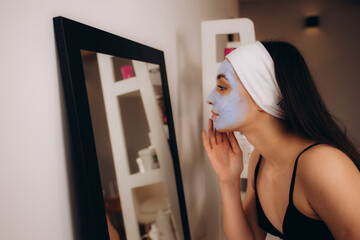 Woman removing facial dried clay mud mask with sponge in bathroom in front of mirror. Skin care....