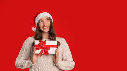 woman with gift box wearing Santa hat on red backdrop