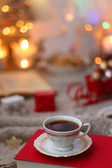 Bowl of cookies, cup of tea, dry oranges, pine cones, books, reading glasses, small presents, various Christmas decorations and lit candles on the table. Cozy Christmas hygge. Selective focus.