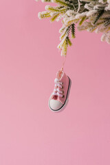 Creative Christmas background with pink sneakers hanging on a green Christmas tree with snow against a pink pastel background. Minimal holiday, New Year, or Christmas concept. - obrazy, fototapety, plakaty