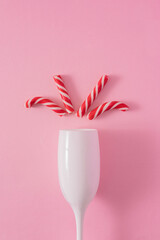 A close-up view of a white champagne glass filled with red Christmas candy cane splashes a pink...