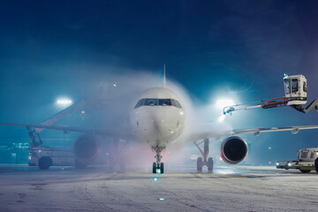 Deicing of airplane before flight. Winter frosty night and ground service at airport during snowfall.. - obrazy, fototapety, plakaty