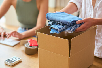 Two Women Friends Running Online Fashion Business Packing Order Of Denim Jeans Up Into Box