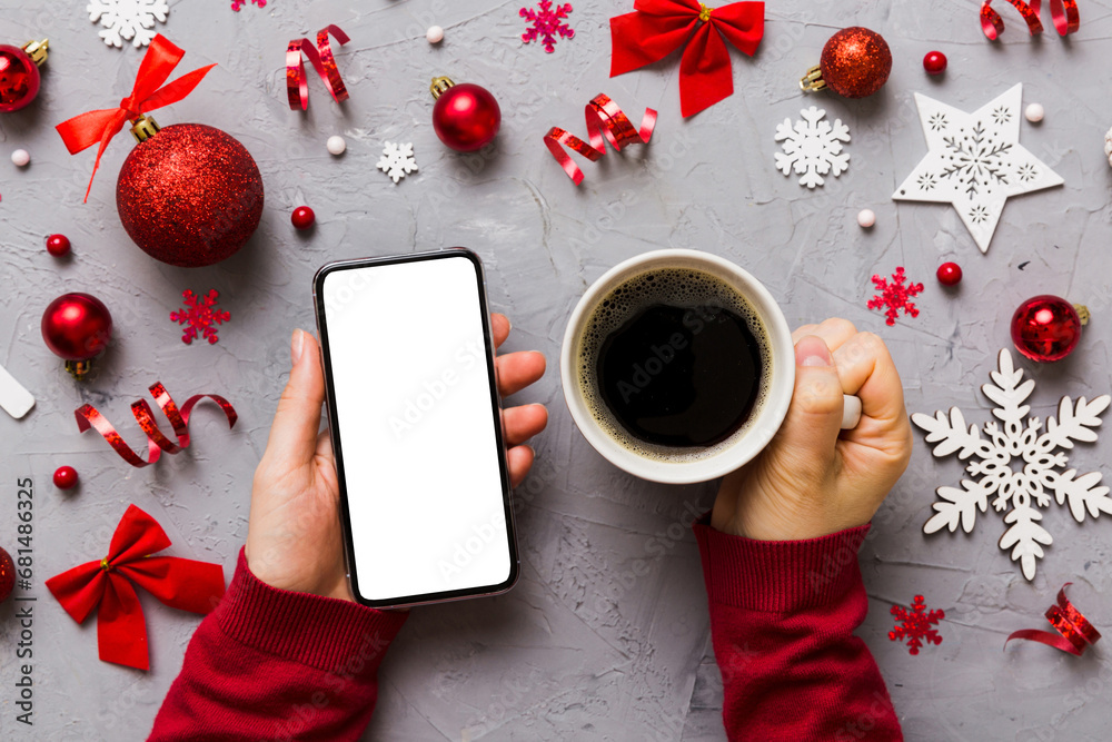 Wall mural above view of female hand holding smart phone with hot cup of coffee. christmas decoration on colore