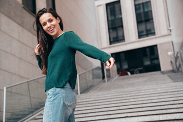 Street fashion portrait of beautiful caucasian woman walking outdoors. Beautiful young model in warm sweater. Fashion stylish pretty female posing in the street, having fun in city. Raising hands