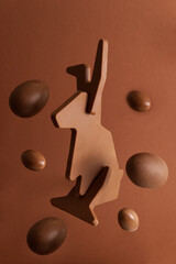 Chocolate Easter bunny levitates with candy Easter eggs on a brown background