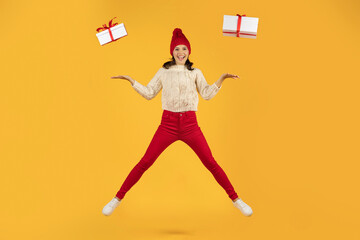 Fototapeta na wymiar woman in knitted cap jumps with two presents, yellow background