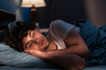 Handsome man sleeping in his cozy bed at night. Attractive guy sleeping profoundly and dreaming at home with blue light. Muslim man asleep with closed eyes.