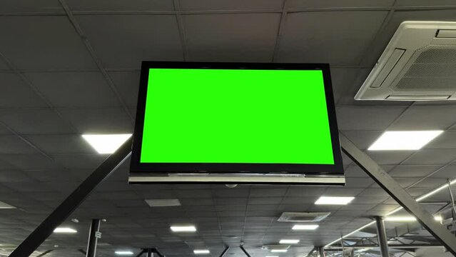 Chromakey green screen on a flat-screen TV, ceiling-mounted in a gym for dynamic content display.