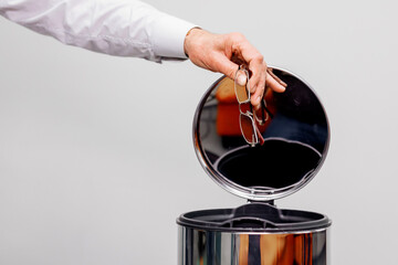 Vision correction concept. Close-up of hand throwing out eyeglasses into trash can.