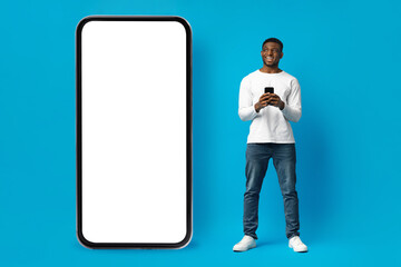Cool black guy in casual outfit standing by huge smartphone