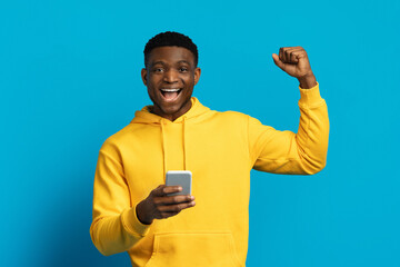 Emotional funny black guy using smartphone gesturing with excitement