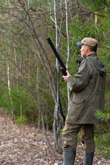 a hunter stands with a gun in his hands in a forest clearing