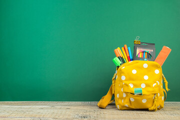 Backpack with different colorful stationery on table. Green background. Back to school.