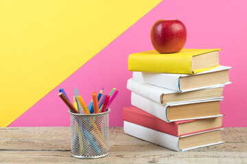 Books stacking. Books on wooden table and pink, yellow background. Back to school. Copy space for ad text.