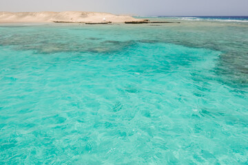 view to a amazing turquoise water and a coral reef with hills from the desert