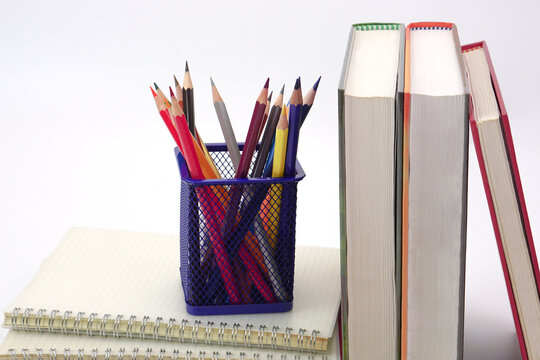 Crayon or colored pencils in box laying on a stack of books, white background. Knowledge and education concept.