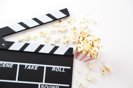 Focus of popcorn and blur clapperboard or movie slate black color on white background. Cinema industry, video production and film concept.