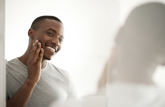 Smiling African man examining his face in a bathroom mirror