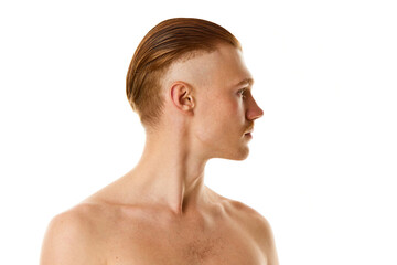 Profile view portrait of young naked man with red hair and stylish haircut against white studio...