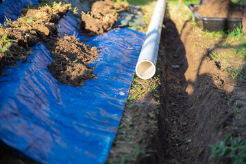 Selective focus plastic sewage pipes PVC, blue tarp with dirt, black mixing tub, pipe ready to...
