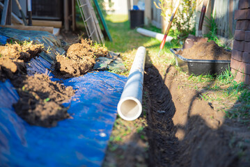 Side of house drainage system installation, PVC pipe ready to laying, buried in ground trench, blue tarp, mixing tub container with dirt, clay soils, residential home, Dallas, Texas, US - obrazy, fototapety, plakaty