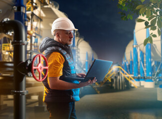 Man industrialist with notebook. Manager inspects night factory. Industrialist near oil storage tanks. Inspector checks oil company. Industrialist man in white helmet on territory of plant