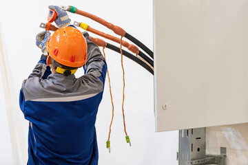 Man installer insulates high-voltage cable. Guy prepares wires to supply electricity. Electrician wraps insulating tape at cable. Electrical engineer with back to camera. Man doing electrical work - obrazy, fototapety, plakaty