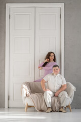 Young happy couple sitting on a sofa in a large studio. Behind them is a large white door. Loving married couple. Cope space for text