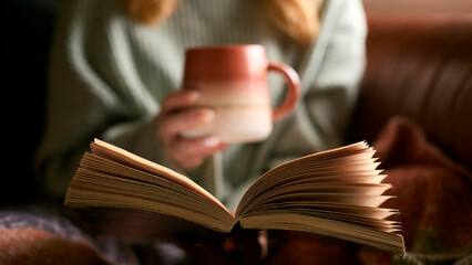 Close Up Of Woman At Home In Winter Jumper With Warming Hot Drink In Mug Reading Book - obrazy, fototapety, plakaty