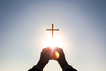 Brightly shining sunlight and silhouette of Christian hands holding high the cross of Jesus Christ symbolizing death and resurrection
