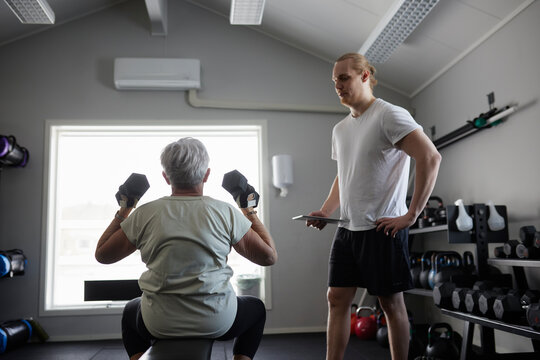 Woman exercising with dumbbell with trainer checking his progress