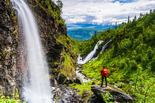 Hiker standing near waterfall in green mountain landscape