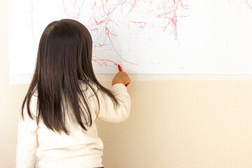 壁のホワイトボードに落書きする女の子の後ろ姿（3歳、日本人）