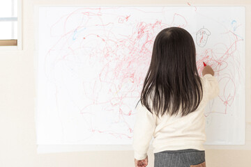 壁のホワイトボードに落書きする女の子の後ろ姿（3歳、日本人）