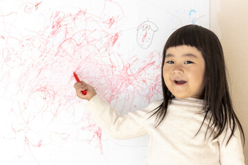 壁のホワイトボードに落書きする女の子（3歳、日本人）