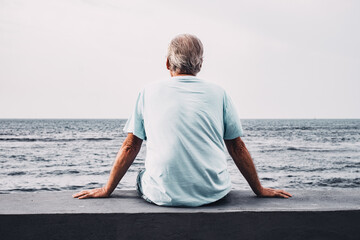 Back view of relaxed senior man sitting face the sea at sunrise looking at horizon enjoying freedom and retirement