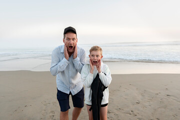 Father and son standing on sandy be ach and making faces