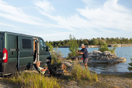 Couple relaxing next to camper van at lakeshore