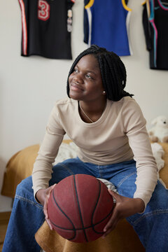 Female teenager holding basketball while day dreaming in bedroom at home
