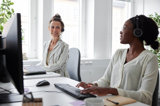 Two women sitting at desk in office and talking to each other