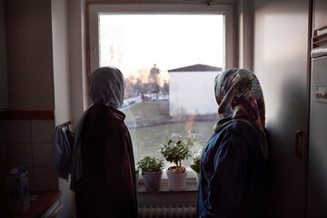 Thoughtful women in headscarves looking through window